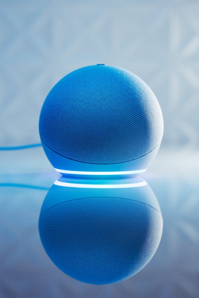 A smart speaker with glowing blue LED lighting and its reflection on a surface.